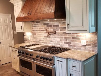 Kitchen with a stainless steel range, wooden hood, and brick-style backsplash.