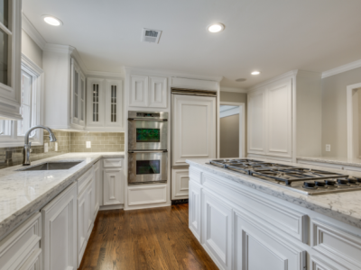 White kitchen with marble countertops, stainless steel appliances, and dark hardwood floors.