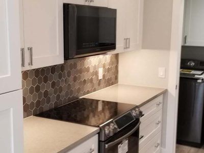 Kitchen with white cabinets, dark tile backsplash, and built-in microwave over a stovetop.