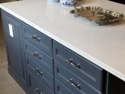 Gray kitchen island with white countertop, silver hardware, and storage drawers.