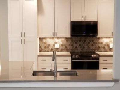 White kitchen cabinets, stainless steel sink and appliances, neutral backsplash.