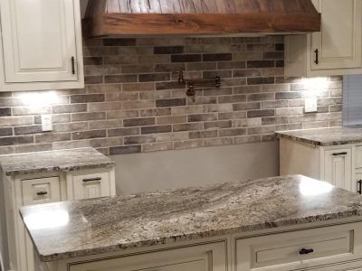 Kitchen with white cabinets, granite countertops, and brick-patterned backsplash. Wooden hood over the stove.