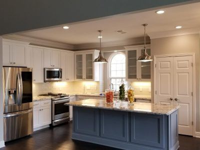 Modern kitchen with white cabinets, stainless steel appliances, and a gray-blue island.