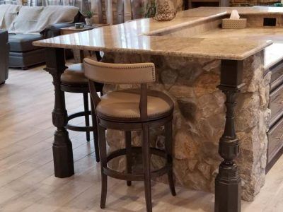 Bar with stone facade and ornate dark legs; two bar stools with leather seats.