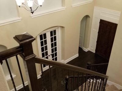 Staircase view from above with dark wood railing, white French doors, and dark wooden door.