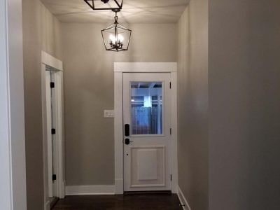 Hallway with a white door, a hanging light fixture, and two doors with white frames and gray walls.