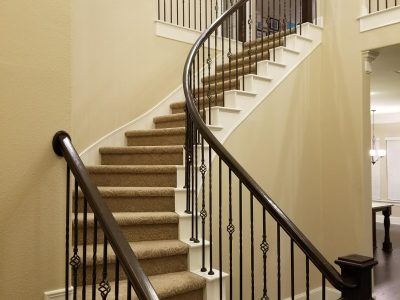 Curving staircase with carpeted steps, black wrought iron railing, and beige walls.