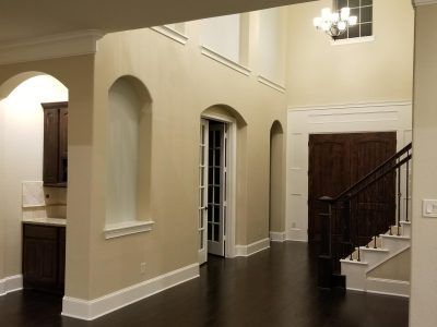 Interior with dark wood floor, arched doorways, a staircase, and a chandelier, all painted in neutral colors.