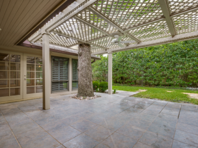 Patio with gray tile floor, latticed ceiling, tree trunk supports, and French doors.