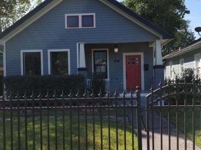 Blue house with red door and small black fence.