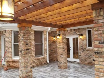 Brick patio with pergola, brick columns, white-trimmed windows and doors, and gray tiled floor.
