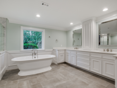 Spacious white bathroom with a freestanding tub, double vanity, and large window overlooking greenery.