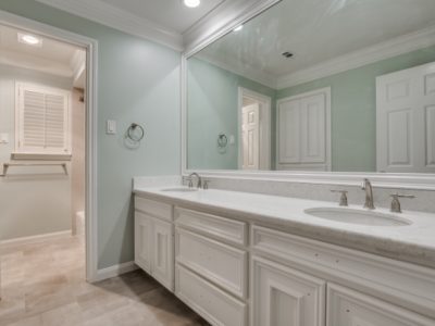 Bathroom with white cabinets, double sinks, large mirror, and pale green walls.