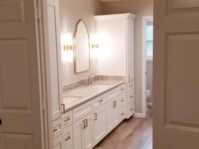 White bathroom with double vanity, gold accents, and tall storage cabinet.