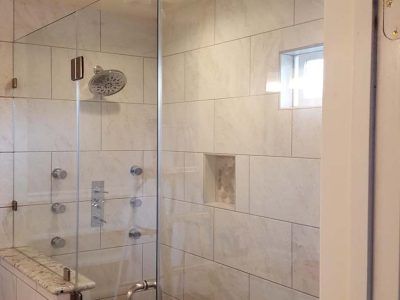 Glass shower enclosure with white tile walls, fixtures, and a small window.