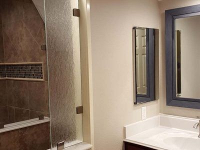 Bathroom with a shower, vanity, and mirror; beige, brown, white color scheme.