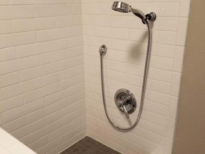 Shower with white tiled walls, chrome shower head, and grey floor tiles.