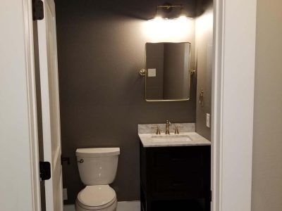 Small bathroom with dark gray walls, white trim, toilet, black vanity with white countertop, mirror, and light fixture.