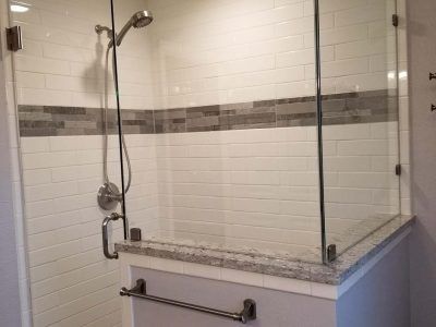 Modern shower with glass doors, white subway tile, and a gray accent band.