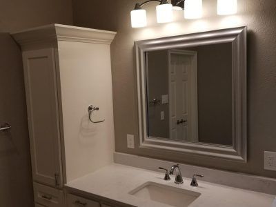 Bathroom with white cabinetry, countertop, sink, and mirror with overhead lighting.