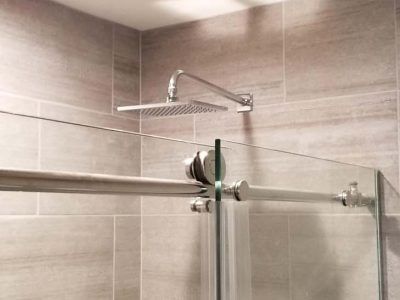 Shower with a square rain showerhead, glass door, and tiled walls.