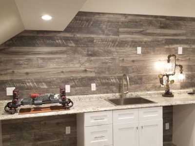 A wet bar with weathered wood paneling, granite countertop, white cabinets, and a decorative lamp.