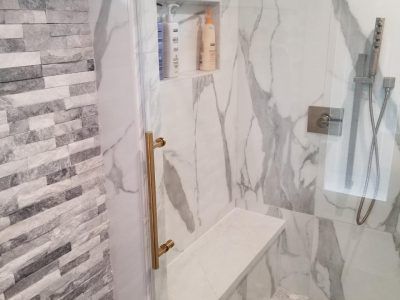Shower with marble walls, stone accent wall, gold fixtures, built-in bench, and shampoo niche.