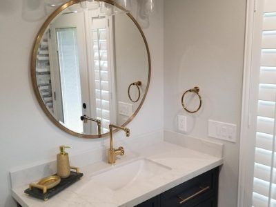 Bathroom vanity with gold fixtures, round mirror, white countertop, and navy cabinet.