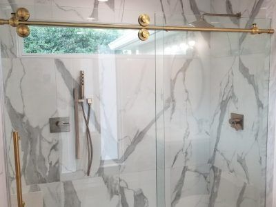 Gold-accented glass shower with white marble-look tile. Sliding door.  Exterior view through a window.