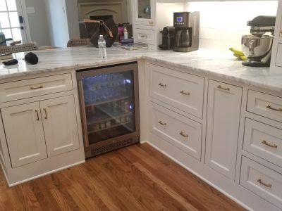White kitchen cabinets with granite countertops. A built-in beverage refrigerator. Hardwood floors.