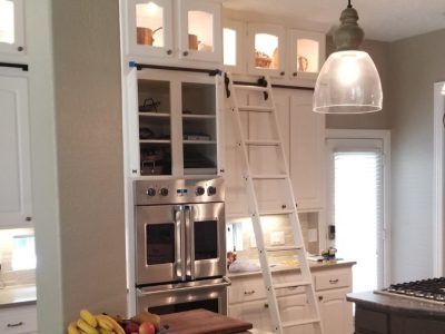 Kitchen cabinets with a tall ladder; a stainless steel oven is below.