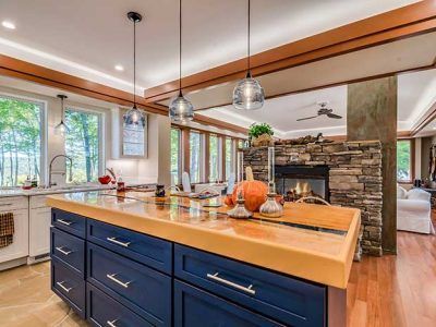 Kitchen island with blue cabinets, wood countertop, pendant lights, and fireplace in background.
