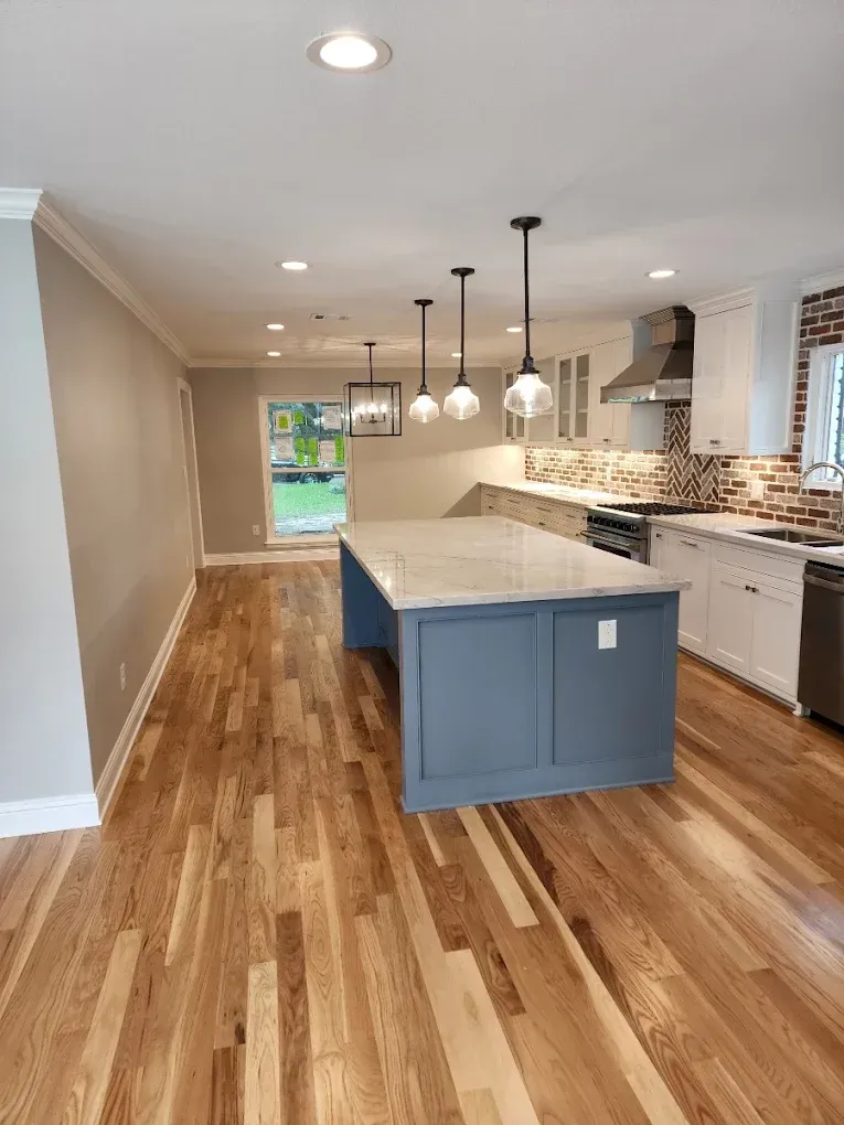 Newly renovated kitchen with wooden floors, blue island, pendant lights, and white cabinetry.