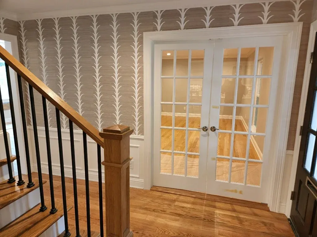 Staircase leading to a room with glass French doors. Beige wallpaper with white pattern; wood floors.