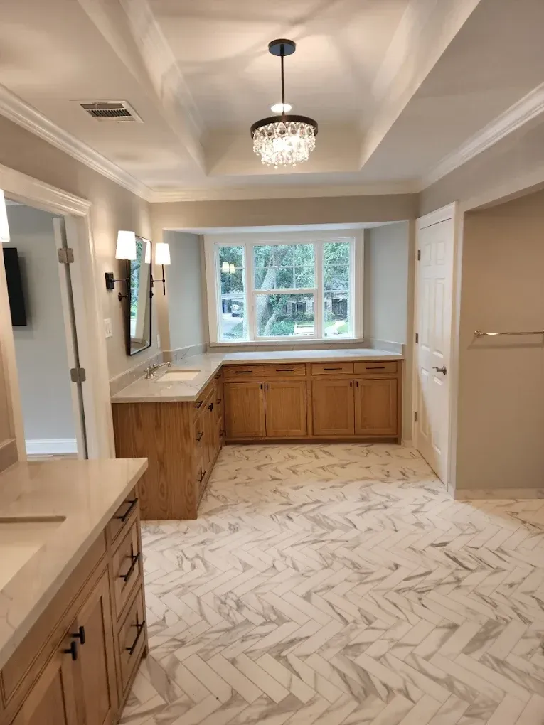 Bathroom with wood cabinets, herringbone tile floor, and a chandelier.