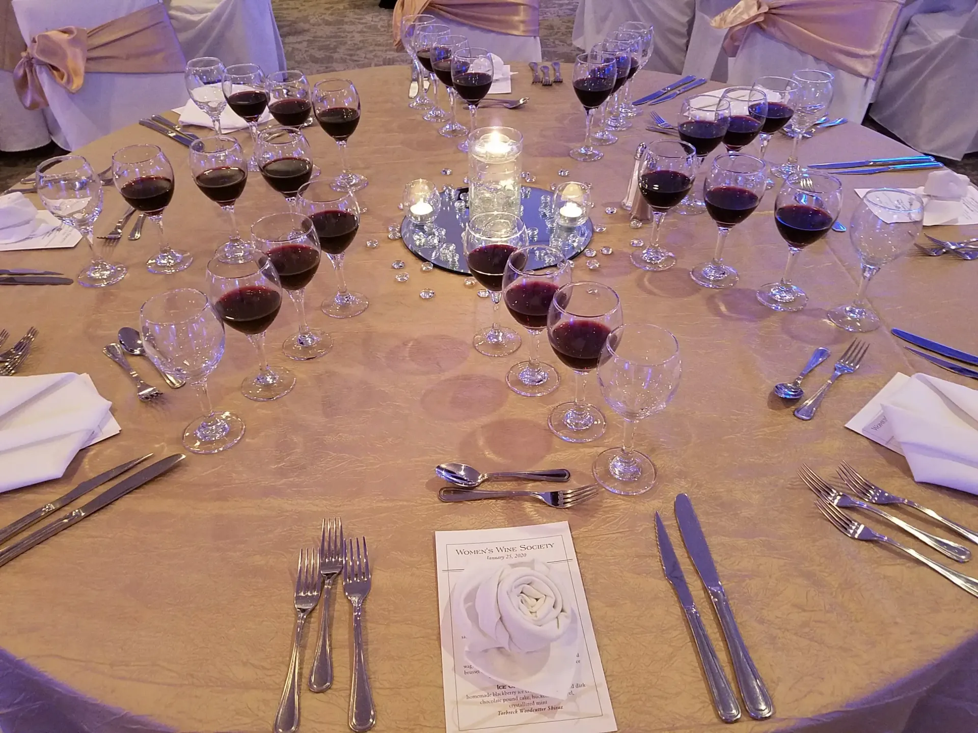 Formal table setting with wine glasses, silverware, and candle centerpiece.