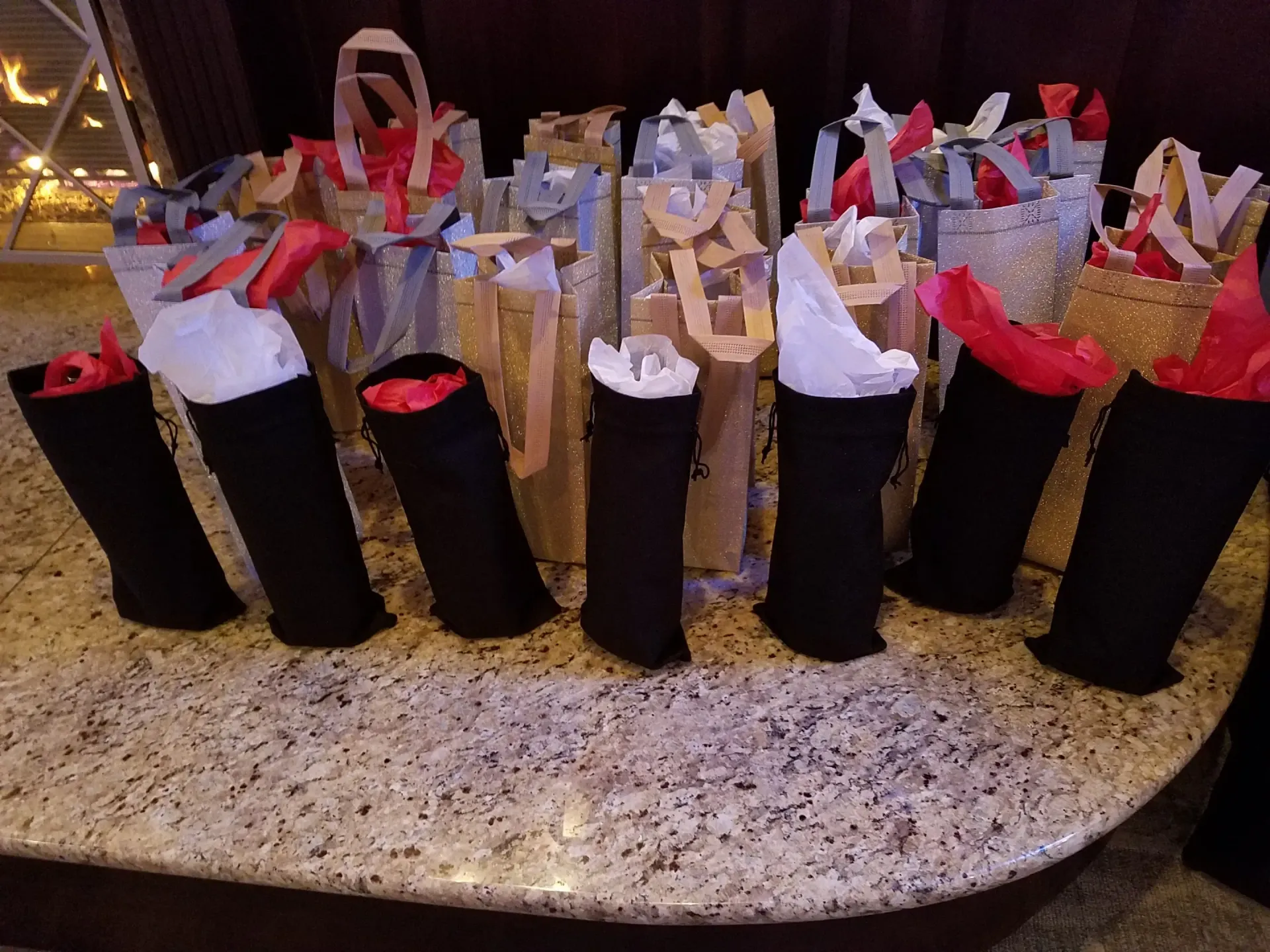 Wine bottles in black fabric sleeves, surrounded by gift bags with red and white tissue paper.