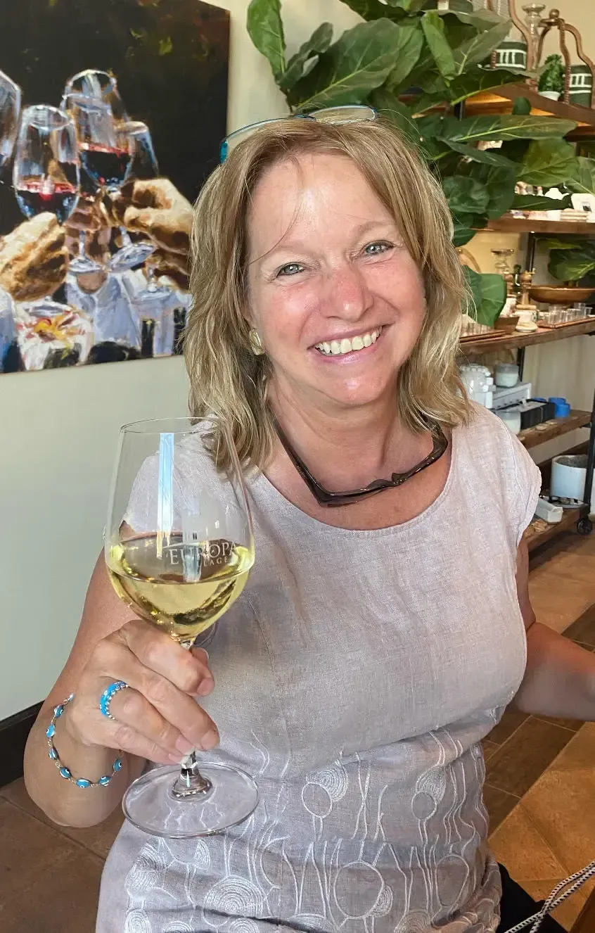 Woman smiling, raising a glass of white wine in a restaurant setting.