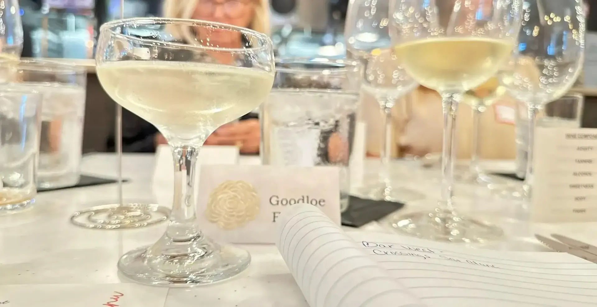 Wine glasses on a table at a tasting. Focus is on a filled, stemmed glass.