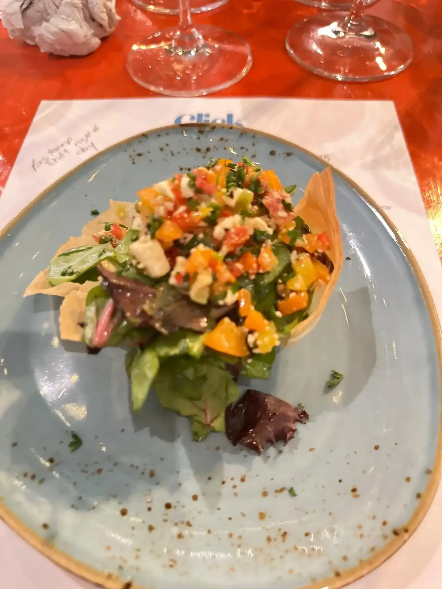 Salad in a crispy bowl on a blue plate, topped with diced vegetables and cheese.