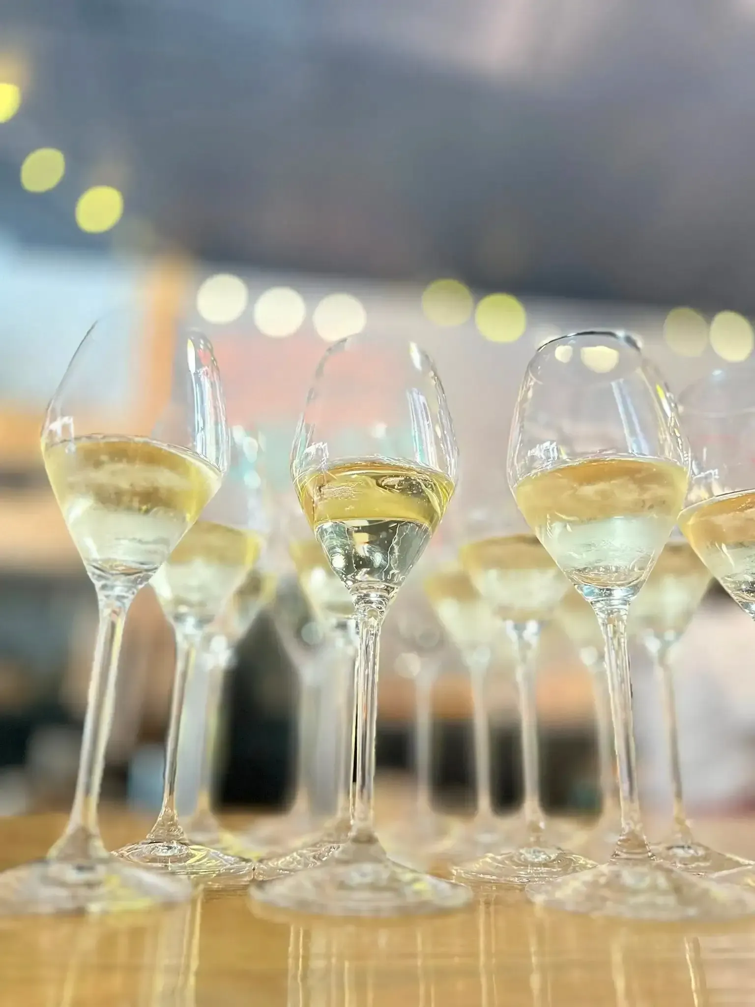 Wine glasses filled with white wine on a wooden surface, with blurred background lights.