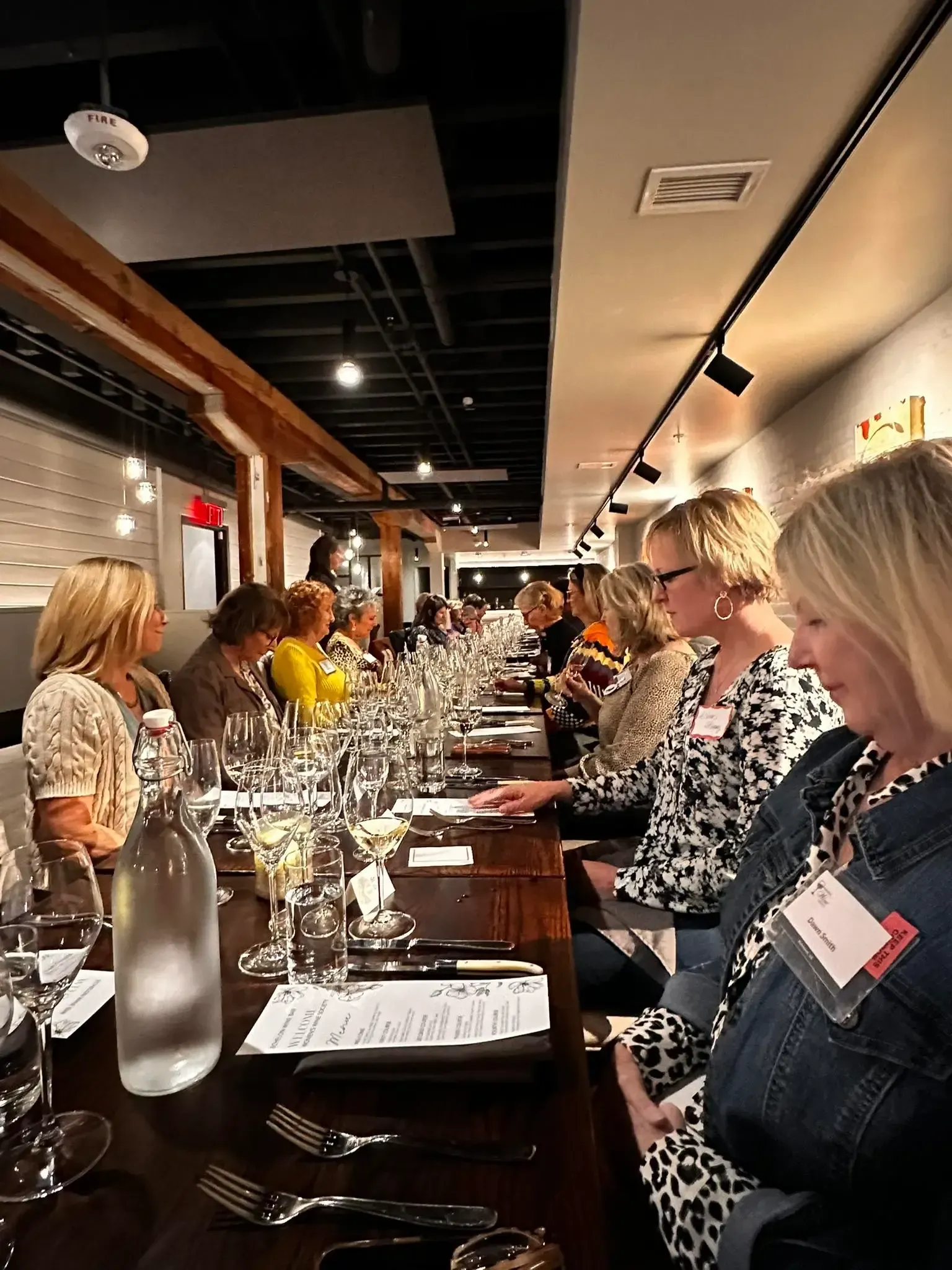 Woman giving a presentation to a group seated at tables in a yellow-walled restaurant.