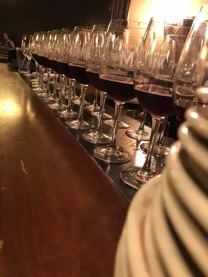 Row of red wine glasses on a bar, illuminated by warm light.