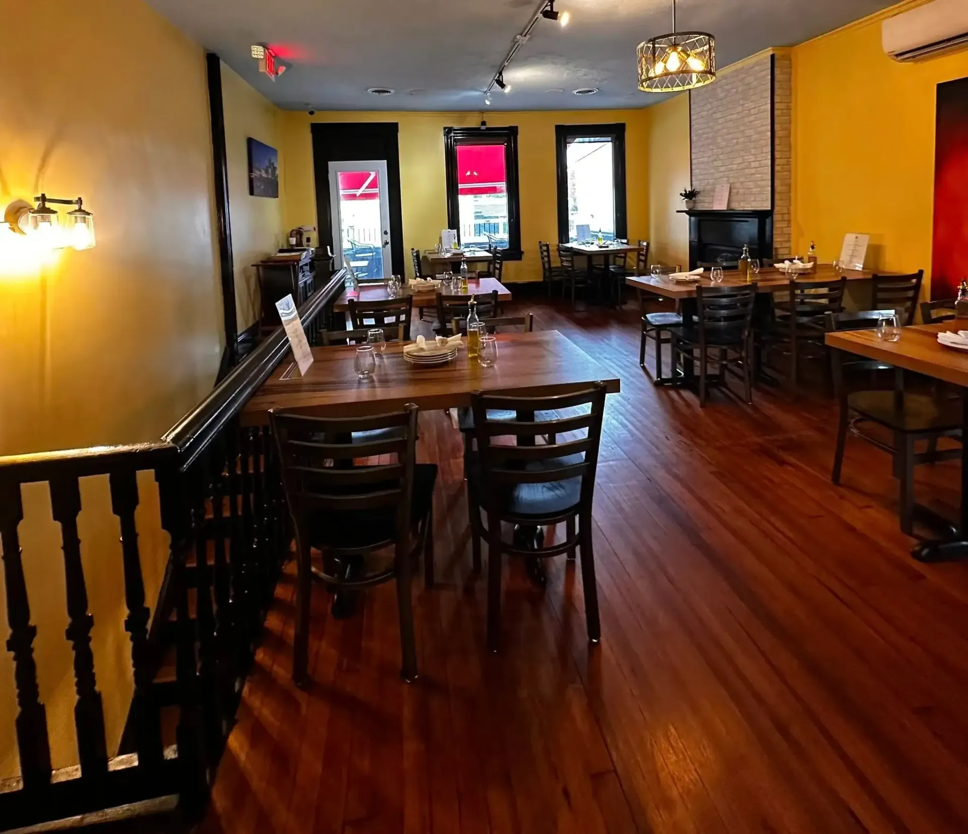 Restaurant interior with wooden floors, tables, chairs, and windows. Yellow and red accents, warm lighting.