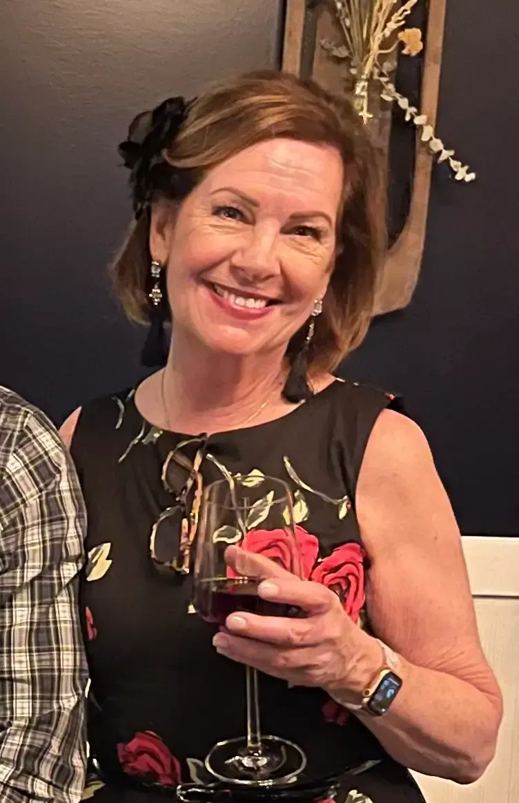 Woman with short brown hair smiles, wearing sparkling earrings and purple sequined top.