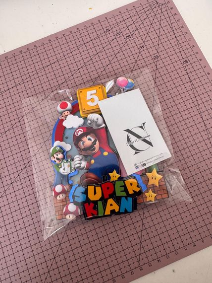 Stickerpakket met Mario-thema op roze ruitjespapier, met een witte kaart en een kleurrijk 
