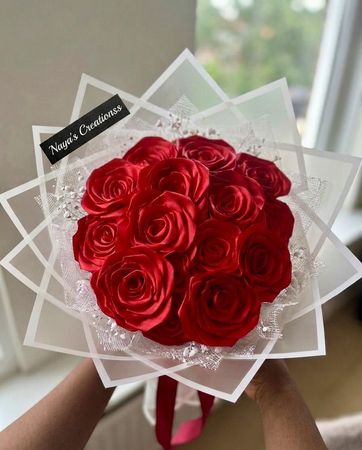 Een boeket rode rozen, verpakt in transparant geometrisch papier, wordt binnenshuis door een hand vastgehouden.