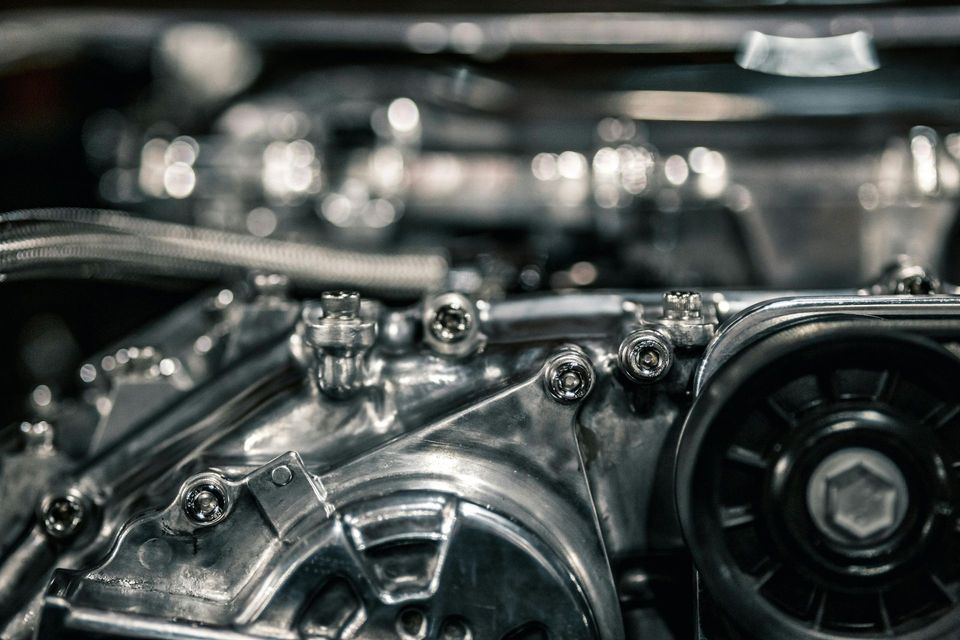 Close-up of shiny metal engine parts with bolts and a belt, in a dim mechanical setting
