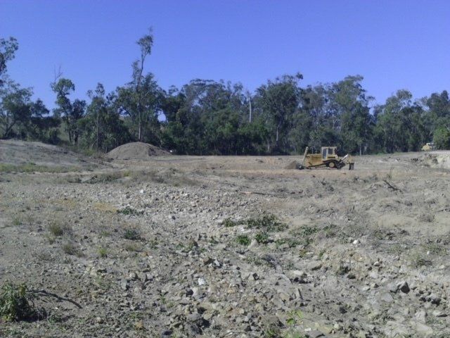 Empty Land With Large Stones And Backhoe — Earthmoving & Excavation Services in Rockhampton, QLD
