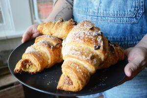 A person is holding a plate of croissants with powdered sugar on them.